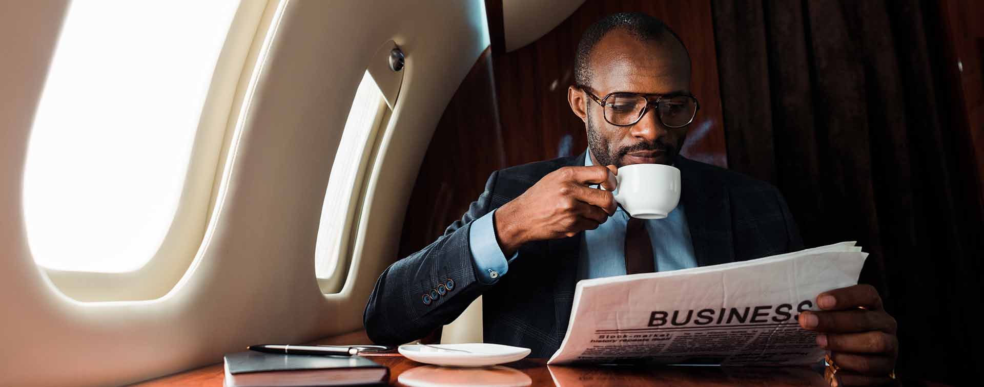 African businessman reading business newspaper while drinking coffee in private plane 