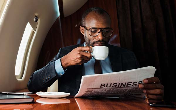 African businessman reading business newspaper while drinking coffee in private plane 