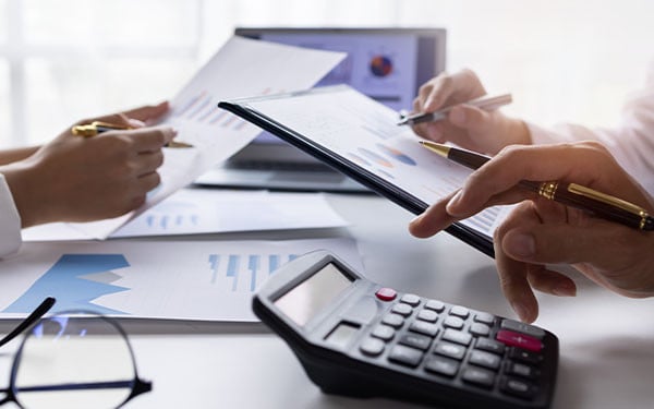 Close-up of financial experts analyzing charts as  one types on a calculator