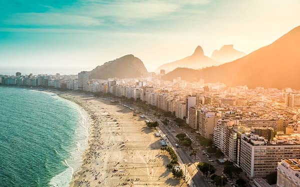 Aerial view of a populated shoreline with a city beside it and mountains in the background.