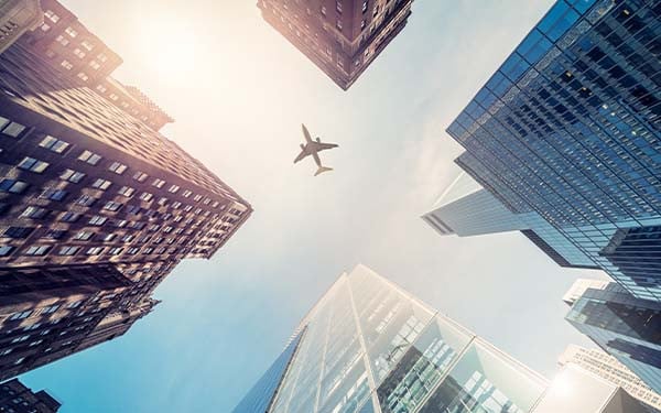 View of skyscrapers from the bottom up with a plane flying overhead.
