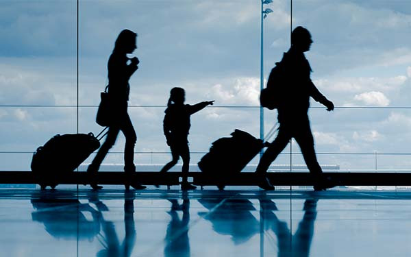 Silhouette of young family with luggage walking at airport, girl pointing at the window