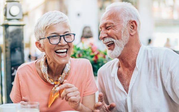An attractive affluent senior couple laughing while sitting outside at a restaurant